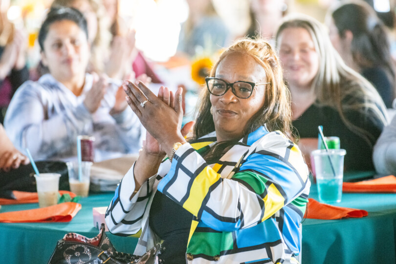 Three women smile and clap hands while seated at a Morrison appreciation event.