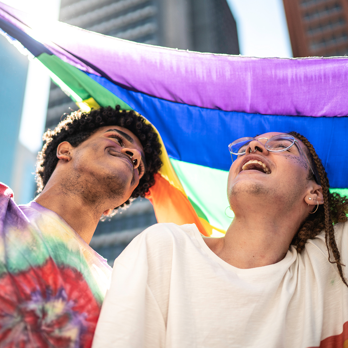 Two young adults under LGBTQ flag