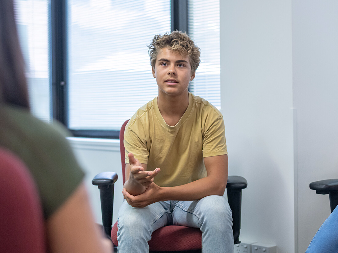 Boy sitting in chair with hand out, speaking